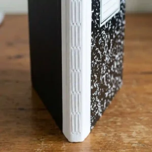 Detailed side view showing the sturdy sewn spine binding of a durable hard bound hard cover composition notebook.