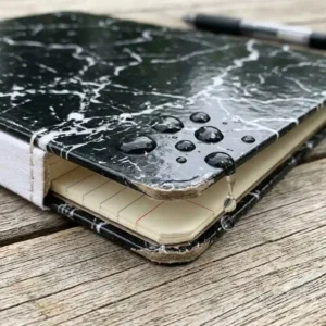 A close-up shot demonstrating the water-resistant surface and thick pages of a premium hard cover composition notebook.